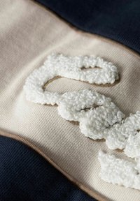 Tessuto intrecciato con colori crema, blu navy e marrone. Ricami bianchi e testurizzati creano un motivo ad anelli su una superficie liscia.