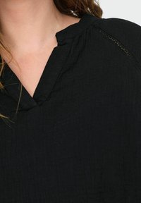 Černý, strukturovaný top s výstřihem do V a jemným krajkovým detailem podél ramenního švu. Měkká, prodyšná látka.
