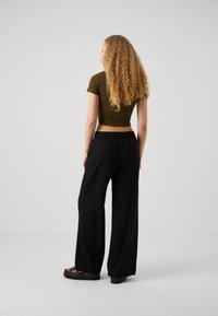Top corto de color verde oliva con mangas cortas, combinado con pantalones negros de corte holgado hechos de una tela ligera, llevados con sandalias negras.