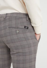 Grå och krämfärgade byxor med rutmönster i texturerad tyg, sidfickor och en bakficka med knapp och varumärkesetikett.