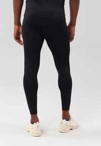 Leggings atléticos pretos feitos de material elástico, design justo, textura suave, com uma cintura ajustada, combinados com sapatos de cor clara.