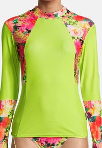 Rash guard à manches longues de couleur vert néon vif, avec des accents de motifs floraux colorés sur les épaules et les manches, fabriqué à partir d'un matériau extensible et léger.