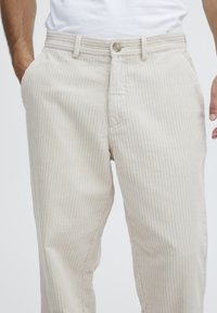 Beige corduroy pants with vertical stripes, featuring a button closure, belt loops, and side pockets. Textured and tailored fit.