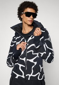 Hoodie mit einem schwarz-weißen Wellenmuster, gefertigt aus einem glatten, leichten Material, mit Reißverschlusstaschen und gerippten Akzenten.