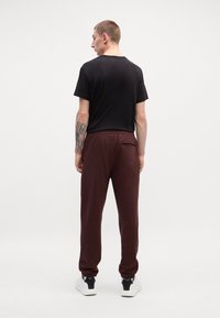 Melnas īsām piedurknēm t-krekls, kombinēts ar bordo treniņbriļļiem, kas aprīkoti ar elastīgu jostasvietu un apakšējām daļām. Apavi - balti sporta apavi.