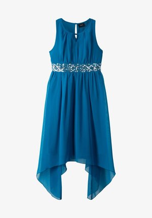 Ragazza con vestito blu senza maniche con dettaglio di cintura argento, che lancia coriandoli dorati, indossa sneakers bianche alte su sfondo bianco.