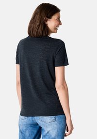 T-shirt noir à manches courtes avec un motif texturé subtil, col rond et coupe décontractée, associé à un jean en denim bleu clair.