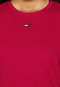 Red athletic t-shirt with a textured pattern and a small, multi-colored logo on the chest area. Round neckline, short sleeves.