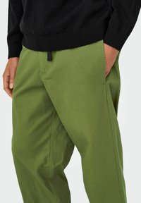 Pantalons en coton vert avec une coupe décontractée, dotés d'une ceinture noire et d'un détail à cordon de serrage. Le tissu a une texture lisse et mate.