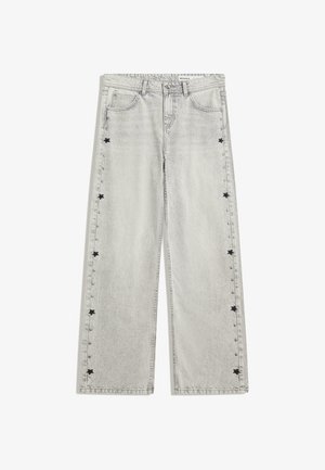 Svetle šedé rovné džíny s černými hvězdnými nášivkami a stříbrnými cvočky podél vnějších švů, na předních kapsách a na poutkách na pás.