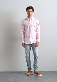 Svetlo roza srajca z dolgimi rokavi in gumbi, s ovratnikom, slim fit kroj, oblečena z svetlo modrimi kavbojkami in svetlo rjavimi supergami.