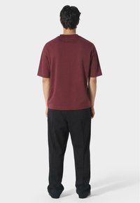 Bordová tričko s krátkým rukávem a volnějším střihem, se zaobleným výstřihem a hladkým povrchem, spárované s černými volnými kalhotami.