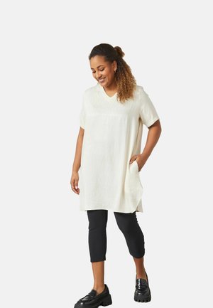 Kort, löst sittande V-ringad tunika i krämfärg med vertikal textur, med korta ärmar och sidfickor, bärs över svarta leggings.