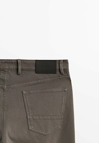 Vue arrière d'un pantalon gris texturé avec une seule poche arrière et une étiquette de marque en cuir noir portant l'inscription "Massimo Dutti" au-dessus de la poche.
