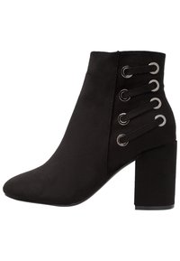 Botín de ante negro hasta el tobillo con puntera afilada, tacón alto tipo bloque y detalle de cordones con ojales metálicos en el lateral.