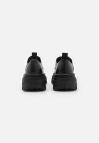Sorte sneakers med en kraftig s�ål, glat syntetisk materiale, forstærket hæl og en trækflap for nem påtagning. Minimalistisk design.