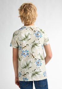 Kortærmet, beige t-shirt med et blomstermotiv i blå og grønne farver med store blade og blomster. Glat tekstur, klassisk pasform.