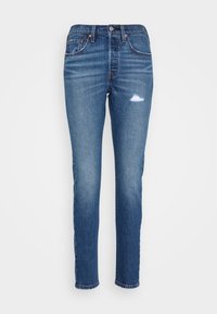 Vaqueros de denim azul con un corte slim, ligeramente desgastados con un patrón de desgastes sutil, diseño de cinco bolsillos y cremallera en la bragueta.