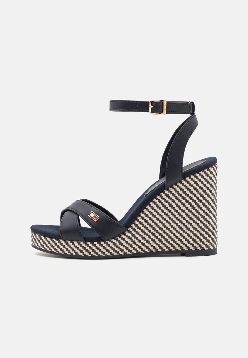 Sandale compensée bleu marine avec bride à la cheville, boucle dorée, brides croisées sur le devant et talon plateforme tissé noir et blanc.