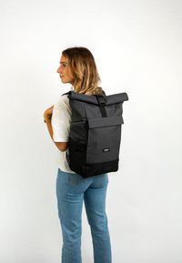 Black roll-top backpack with a gray fabric outer, a front pocket, and adjustable straps, featuring a minimalistic design and logo detail.