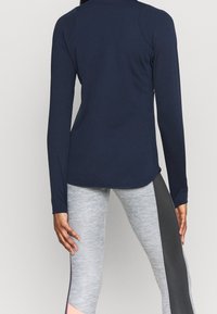 Top azul marino de manga larga con textura suave, combinado con leggings gris claro que tienen paneles laterales en gris oscuro y rosa para contraste.