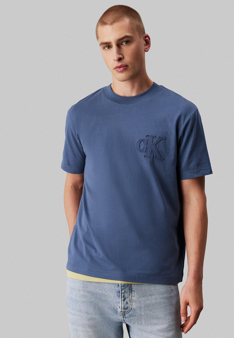 T-shirt in cotone blu con scollatura rotonda e maniche corte, caratterizzata da un logo CK ricamato sul petto sinistro. Vestibilità casual, texture liscia.
