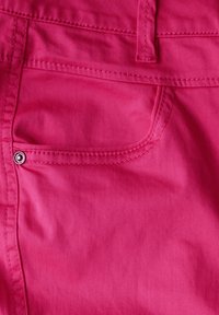 Jean en coton fuchsia avec une texture lisse, présentant une poche arrière avec un bouton poussoir argenté et des détails de couture visibles.