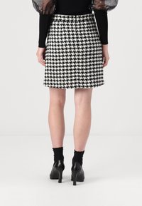 Rutigt mönstrad kjol i svart och vitt, tillverkad av texturerat tyg, med en åtsittande silhuett och en klassisk nederkant. Svarta klackskor synliga.