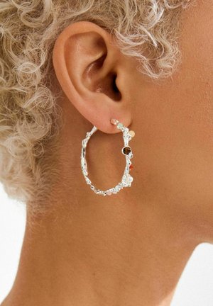 Silver hoop earring featuring a textured design with multicolored bead accents, including white, brown, and peach tones.