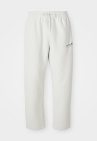 Pantalons de survêtement gris clair en tissu doux, dotés d'une taille élastique avec cordon de serrage et d'un petit logo sur la cuisse gauche.
