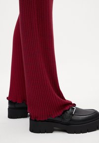 Scarpe con la piattaforma nera e dettagli con fibbia abbinate a pantaloni svasati a righe rosse e navy con orlo ondulato. La trama appare a costine.
