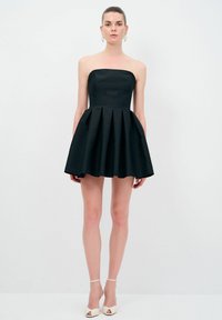 Svart axelbandslös klänning med en figurnära bodice och en plisserad kjol. Slät textur, över knä-längd, kombinerad med vita högklackade skor.