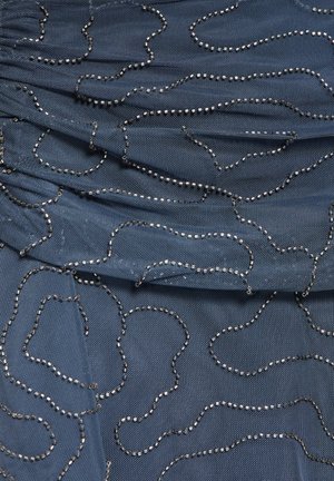 Modrá látka so zloženou textúrou zdobená nepravidelnými striebornými korálkovými líniami vytvárajúcimi abstraktné slučkové vzory po celej ploche.