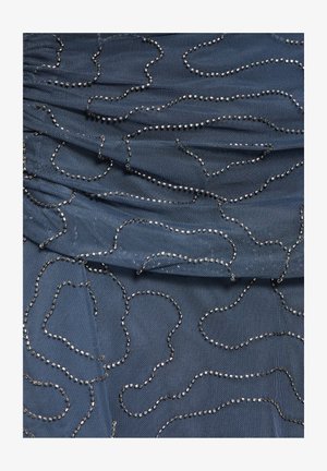 Blauer Stoff mit gefalteter Textur, dekoriert mit unregelmäßigen silbernen Perlenlinien, die abstrakte geschlungene Muster über die Oberfläche schaffen.