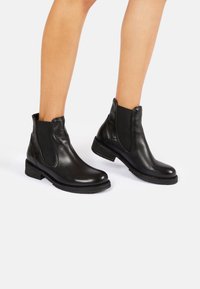 Botas de tobillo de cuero negro con paneles elásticos laterales, puntera redondeada y tacón bajo apilado. La suela tiene un acabado texturizado para un mejor agarre.