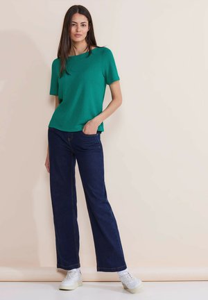Green short-sleeve top with a relaxed fit, paired with dark blue wide-leg jeans and white sneakers. Smooth fabric and simple design.