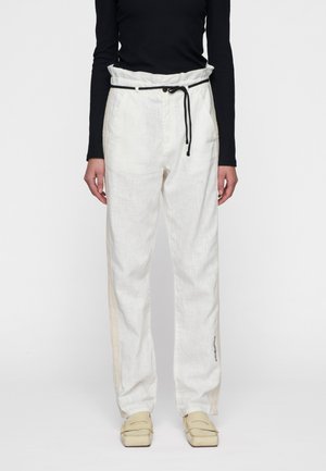Pantaloni leggeri bianchi in misto lino con vita regolabile, tasche laterali e dettagli beige che scorrono lungo le cuciture esterne. Texture morbida.
