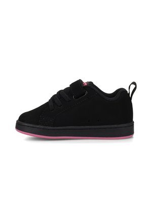 Schwarzer flacher Sneaker mit Schnürung und Klettverschluss, pinke Akzente auf Zunge und Sohle sowie einer Zuglasche hinten, vor weißem Hintergrund.