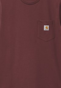 Camiseta de algodón burdeos con cuello redondo y mangas cortas. Presenta un bolsillo en el pecho izquierdo y un parche de logo cuadrado.