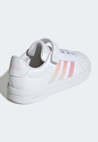 Bílá sportovní bota s vrchním dílem ze syntetické kůže, páskem na suchý zip a třemi duhovými pruhy. Rovná gumová podrážka a jemné logo na patě.