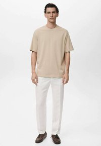 Tricou din bumbac bej cu decolteu rotund, asortat cu pantaloni drepți albi și pantofi din piele maro. Design simplu, modern.