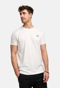 Hvid bomulds t-shirt med rund hals, korte ærmer og et lille grafisk print på brystet. Blød tekstur, afslappet pasform.