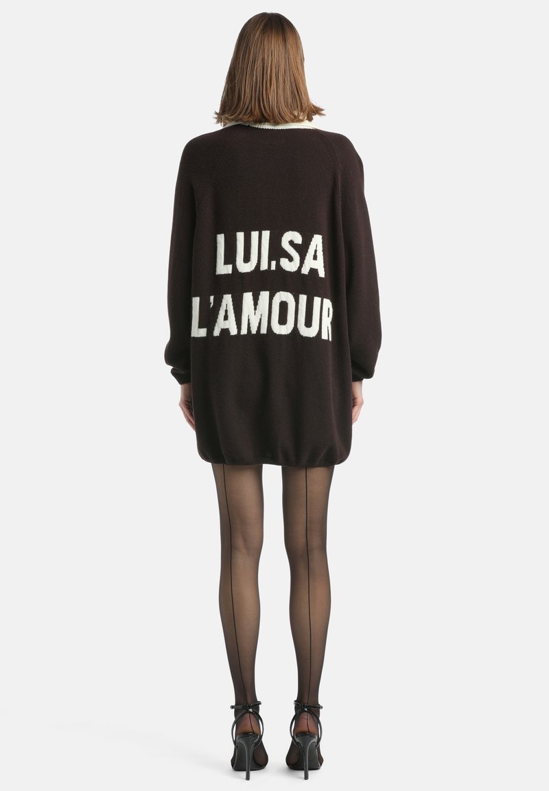 Hnedý pletený sveter s voľným strihom, na chrbte s bielym textom "LUI.SA L'AMOUR", so žebrovanými okrajmi a mäkkou textúrou. Transparentné pan�čuchy dokončujú vzhľad.
