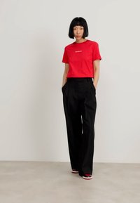 Red cotton T-shirt with a crew neck and white text, paired with black high-waisted wide-leg trousers and black and red sneakers.