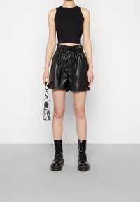 Černý krátký top ve stylu tílka ve spojení s černými kraťasy z umělé kůže s vysokým pasem a páskem na zavazování. Černé boty na šněrování a vzorovaná taška doplňují vzhled.