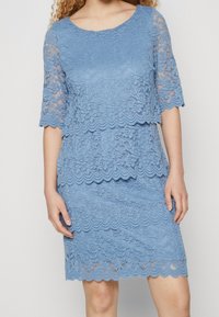 Robe en dentelle bleu clair avec des bords festonnés. Dotée de manches mi-longues et d'une texture superposée avec des motifs floraux tout au long.