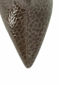 Spitze eines braunen Lederschuhs mit Krokodilprägung und sichtbarer zentraler Naht auf weißem Hintergrund.