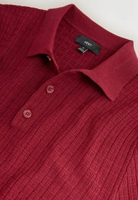 Polo shirt texturé bordeaux doté d'un col côtelé, d'une patte de boutonnage à deux boutons et d'un motif géométrique subtil sur le tissu. Étiquette de la marque visible.