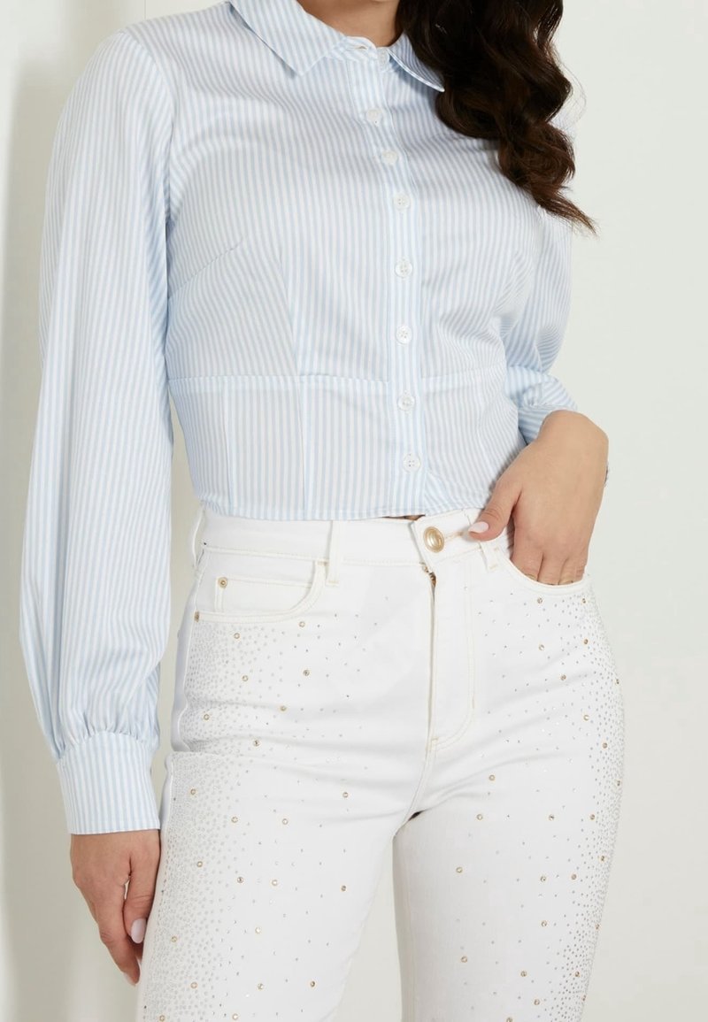 Light blue and white striped collared blouse with long sleeves, paired with white denim jeans featuring metallic studs and a fitted design.