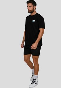 Camiseta negra de manga corta con un gráfico colorido en el pecho, combinada con pantalones cortos negros y zapatillas blancas.